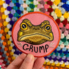 Patch with a toad design and 'GRUMP' text held in front of a colourful background