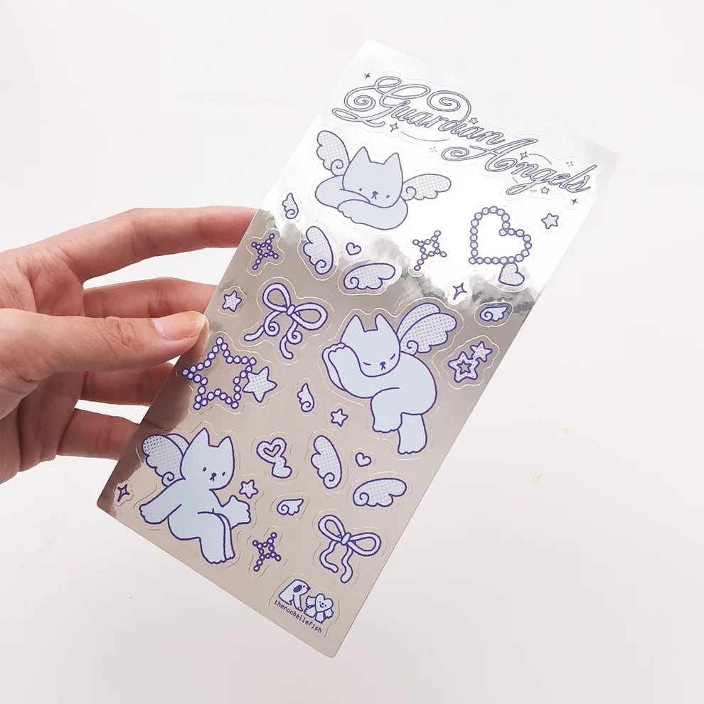 A hand holds a clear metallic silver sticker sheet decorated with cute purple angel illustrations, including winged cats, bows, stars, and hearts, against a plain white background.
