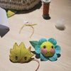 Two handmade felt flower and leaf crafts on a wooden table, with thread, paper, and crafting supplies scattered around them.