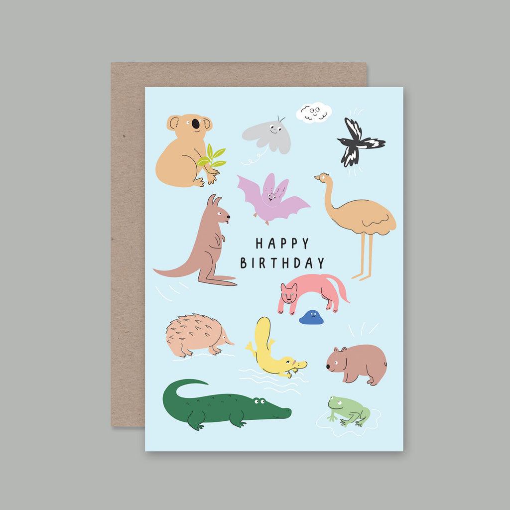 A light blue Australian-themed birthday card with cute animal illustrations and the words 'HAPPY BIRTHDAY' in the center, shown with a brown kraft envelope behind it on a neutral grey background.