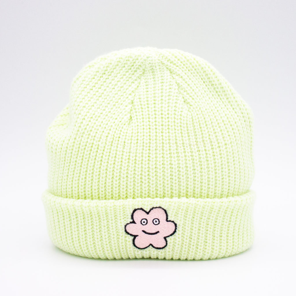 Front view of a Lime wide knit beanie with a folded brim, featuring a smiling embroidered flower patch on the front, displayed against a plain white background.