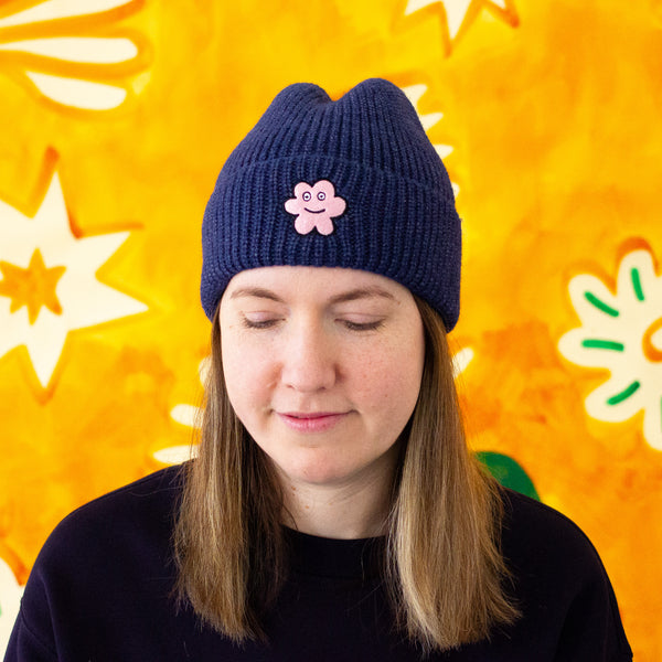 Person wearing a dark navy knit beanie with a pink flower design against a colorful background