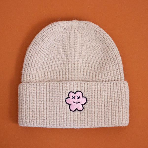 Oatmeal coloured beanie with a pink embroidered patch featuring Happy Luci. 