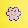 A die-cut sticker featuring a cute flower shaped character with a holographic border, set against a plain yellow background.