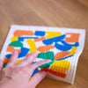 Picture of a hand using the harvest dishcloth to wipe a bench. 