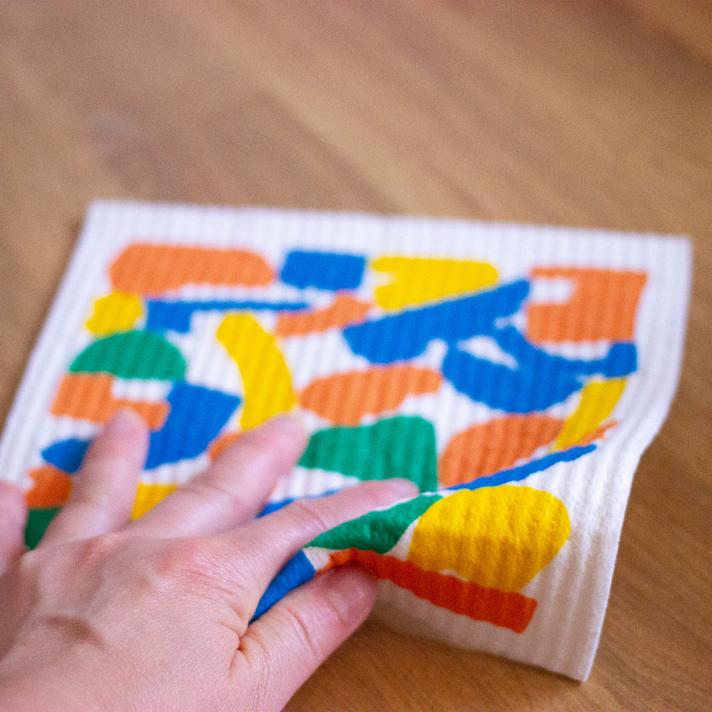Picture of a hand using the harvest dishcloth to wipe a bench. 