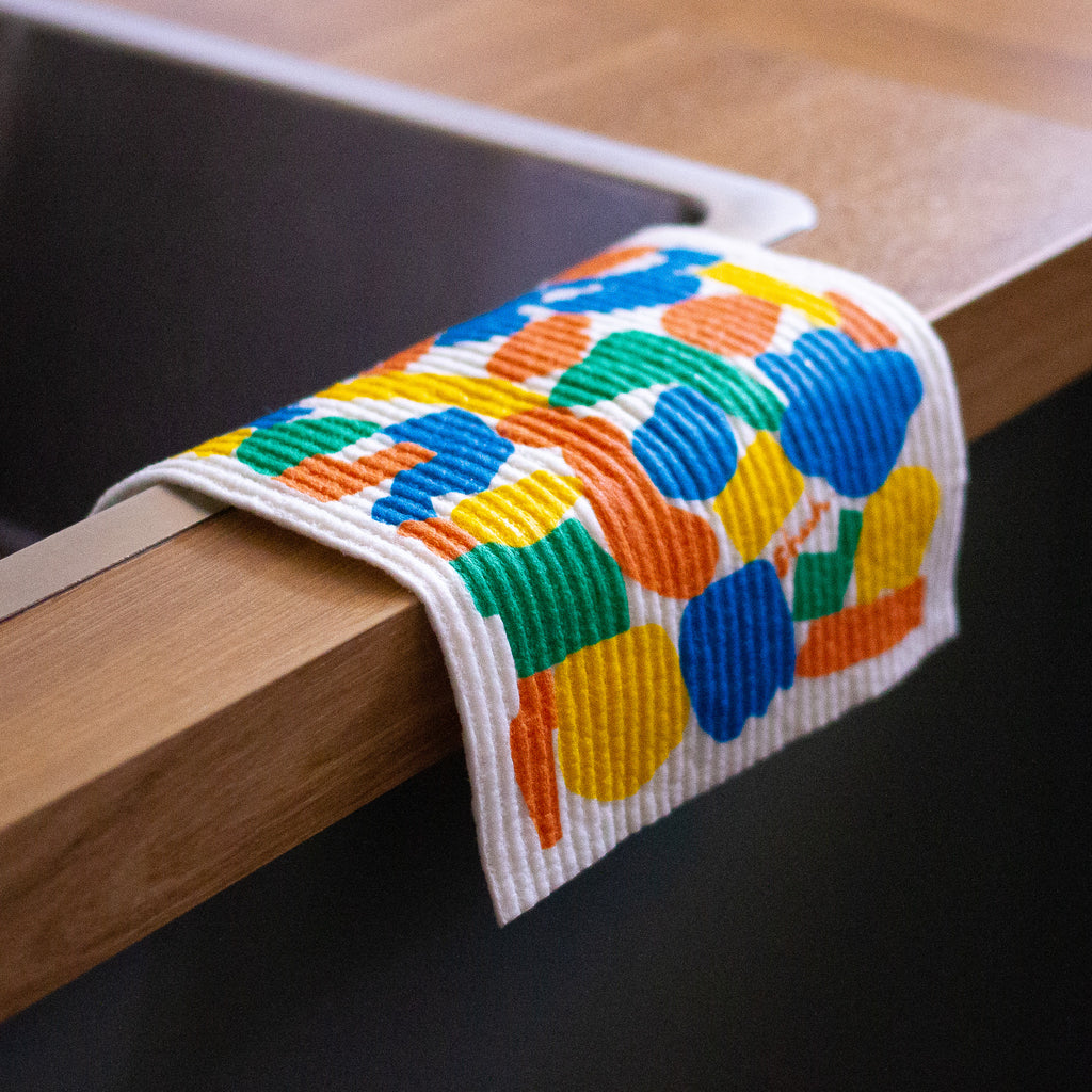 In use picture of the shuh and spruce dishcloth, with cloth hanging off the side of a sink. 