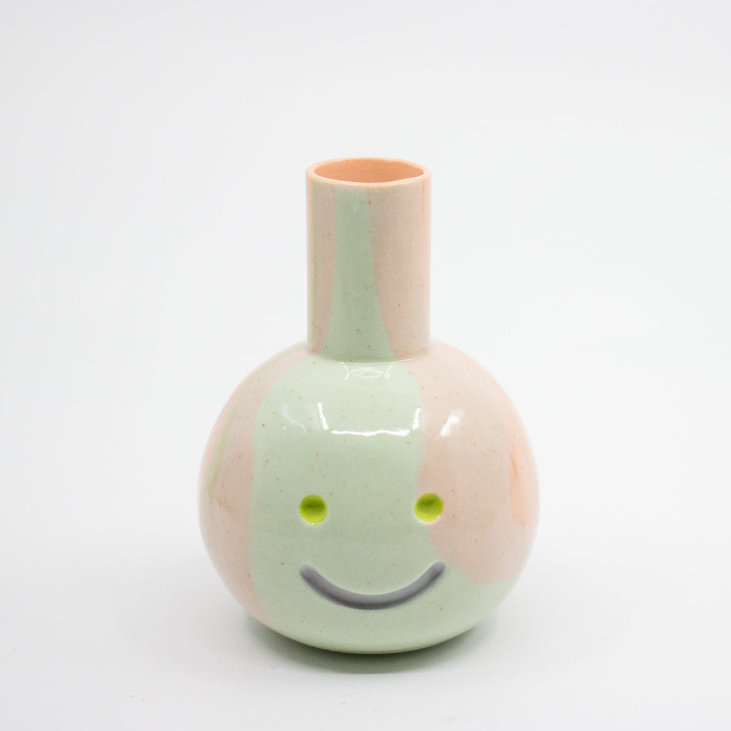 Small ceramic vase with a face design on a white background