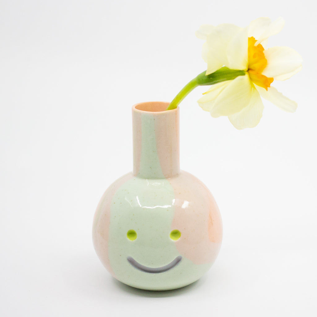 Smiley face ceramic vase with a flower on a white background