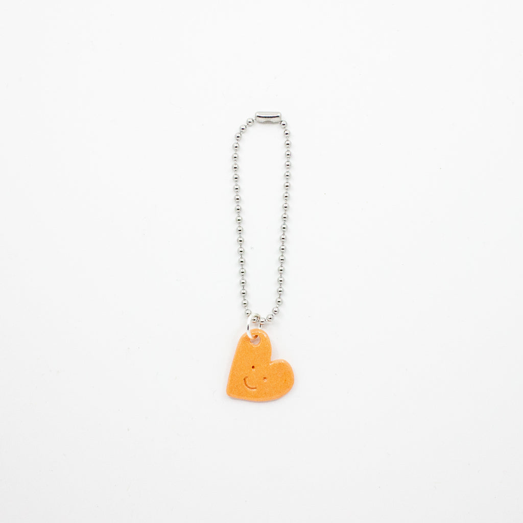 Orange heart-shaped charm with a metal chain on a white background