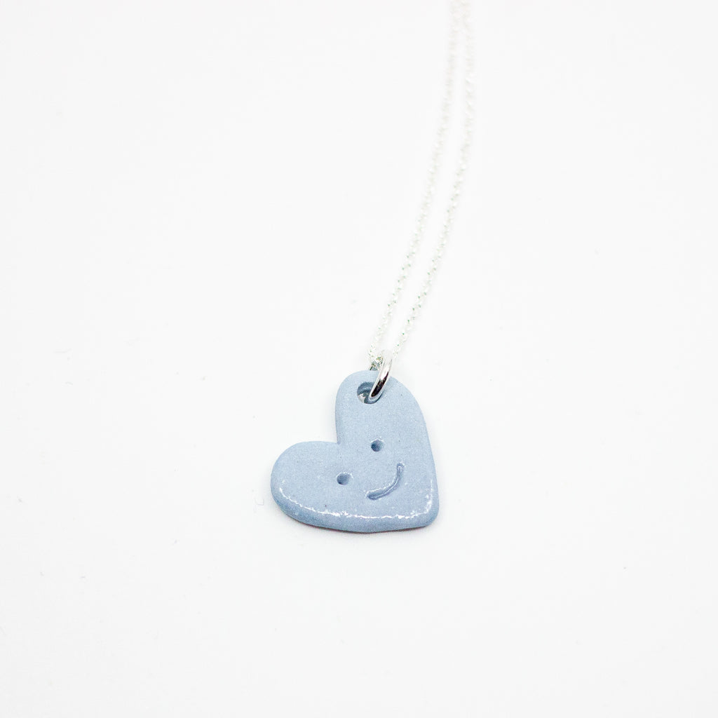 Blue heart-shaped necklace with a smiley face on a white background