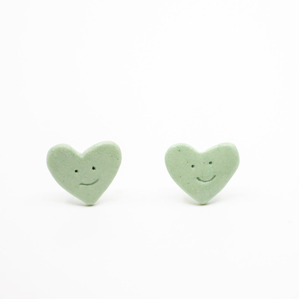 Two green heart-shaped smiley face objects on a white background