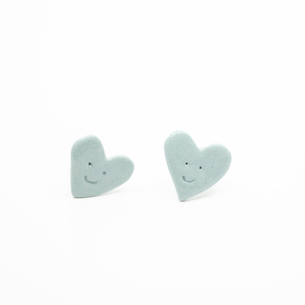 Two sky blue heart-shaped earrings with smiling faces on a white background
