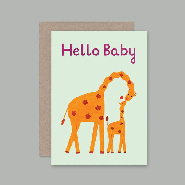 A baby greeting card with a kraft envelope, featuring an illustration of a mother giraffe and baby giraffe with the text 'Hello Baby' in pink on a pale mint background.