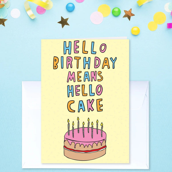 A yellow greeting card with the phrase 'HELLO BIRTHDAY MEANS HELLO CAKE' in multicoloured letters above a birthday cake illustration, shown with a white envelope on a light blue background with confetti and star decorations.