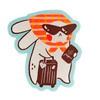 A cute cartoon bunny character sticker with a red and orange plaid scarf, sunglasses, holding a brown suitcase and a passport, on a white background with a light blue outline.