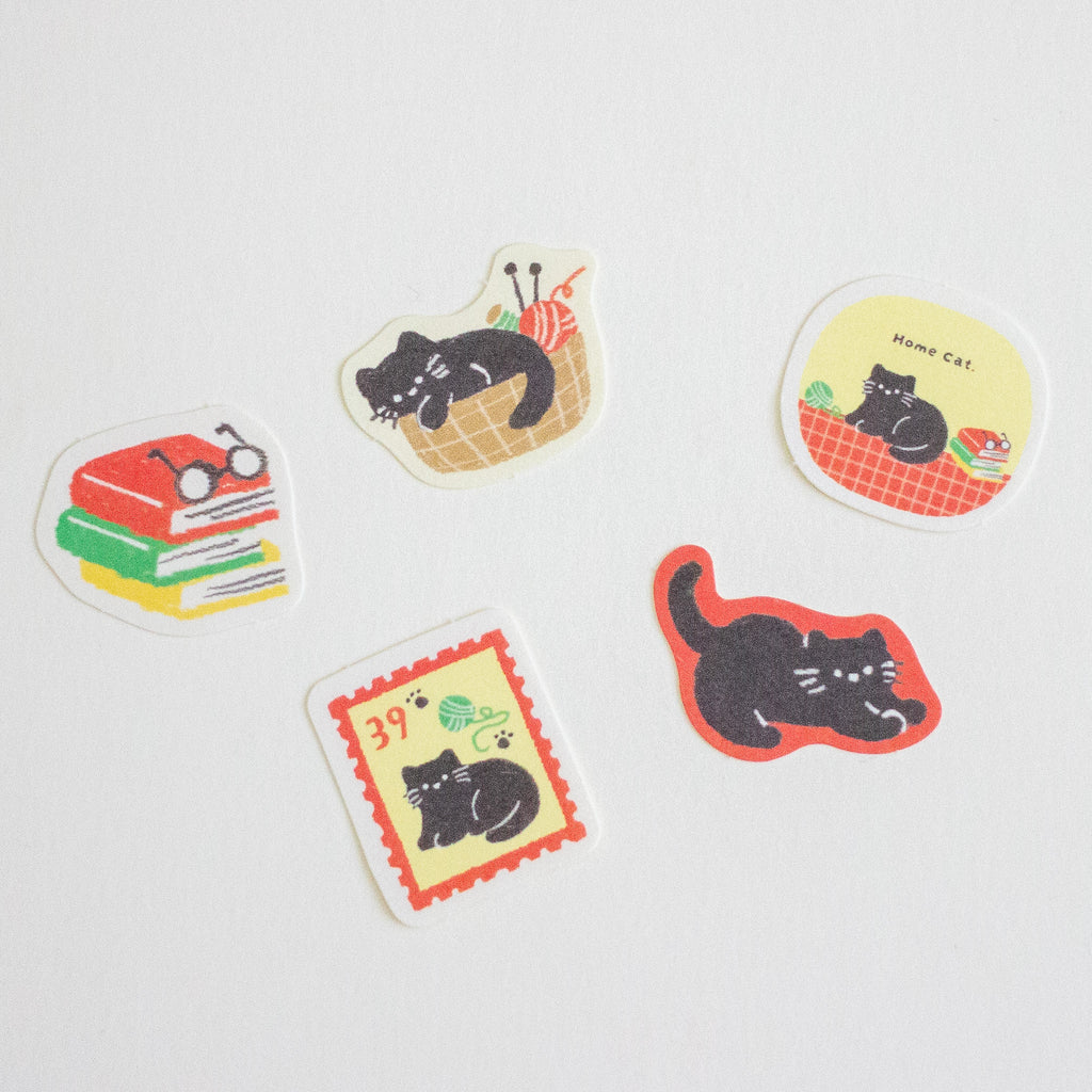 Five cute cat-themed stickers with white borders scattered on a light grey background. The designs include a stack of books with glasses, a cat in a basket, a cat on a red checkered mat with the words 'home cat', a postage stamp-style cat illustration, and a black cat silhouette with red border.