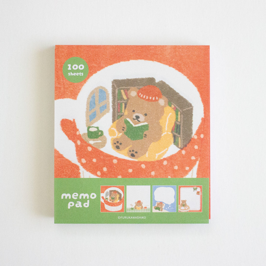 A square memo pad with a warm orange cover featuring an illustration of a teddy bear reading a book, with a green band at the bottom labeled 'memo pad' and small sample note areas.