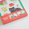A close-up of a memo pad package featuring a white background with a black cat illustration, colourful books and cup graphics, and a coral-red lower band labeled 'memo pad'.