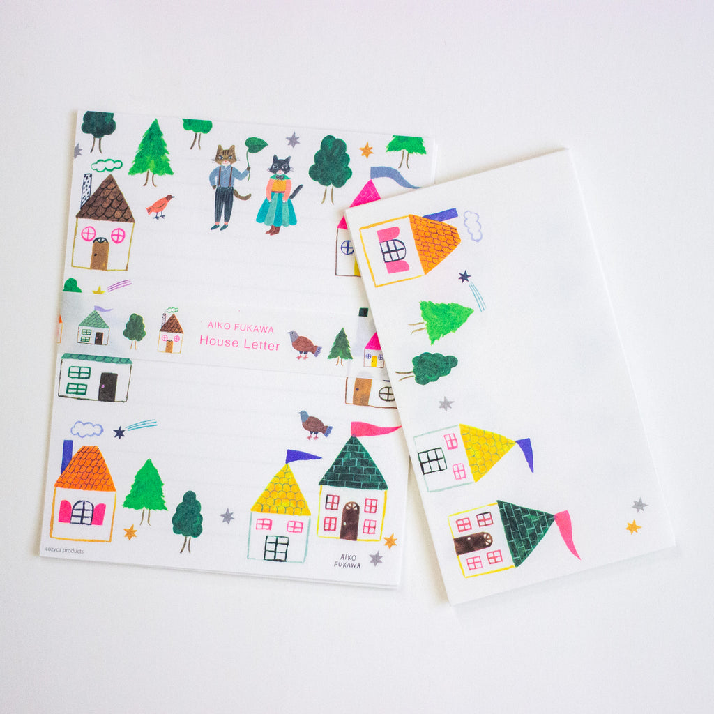 A set of illustrated stationery pieces on a white background, including a house letter template and matching decorative cards or envelopes with colorful house, tree, bird, and star drawings.