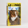 A 500-piece jigsaw puzzle box by Le Puzz featuring a close-up photo of a tabby and white cat wearing a white hat, set against a yellow border on a light grey background.