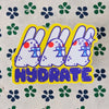 A die-cut sticker featuring three cartoon white rabbits holding blue drinks with red cheeks, outlined in yellow, with the word 'HYDRATE' in purple bubble letters below. The sticker is placed on a light beige background with a repeating pattern of dark blue and green clover.