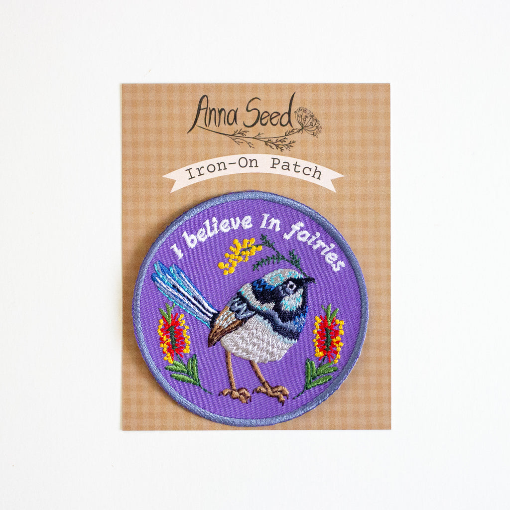 Iron-on patch with a bird design and 'I believe in fairies' text on a brown backing card, branded Anna Seed.