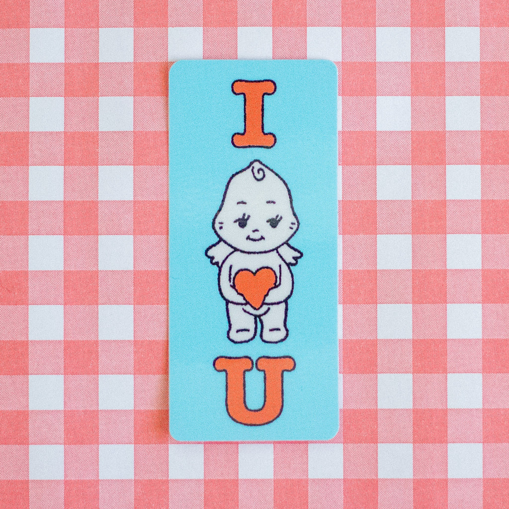 A rectangular light blue sticker featuring a cute cartoon baby character holding an orange heart, with the letters 'I' and 'U' in orange above and below, placed on a pink and white checkered background.