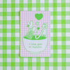 A rectangular pink and white gingham sticker featuring a green line-art illustration of two rabbits in a bowl with hearts and the text 'i love you so matcha', placed on a green and white checkered background.