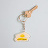 A keychain featuring a fried egg illustration with the text 'I'M JUST AN EGG BOI' on a light blue background, attached to a silver keyring with a key.