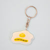 A keychain featuring a fried egg illustration with the text 'I'M JUST AN EGG BOI' on a light blue background, attached to a silver keyring with a key.