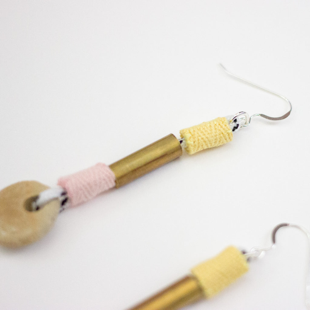 Pair of earrings with brass, ceramic and fabric highlights on a white background