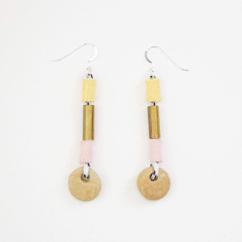 Pair of earrings with brass, pink and yellow fabric, and beige ceramic elements on a white background