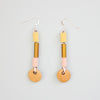 Pair of earrings with brass and pink and yellow fabric highlights, and ceramic beads on a light gray background