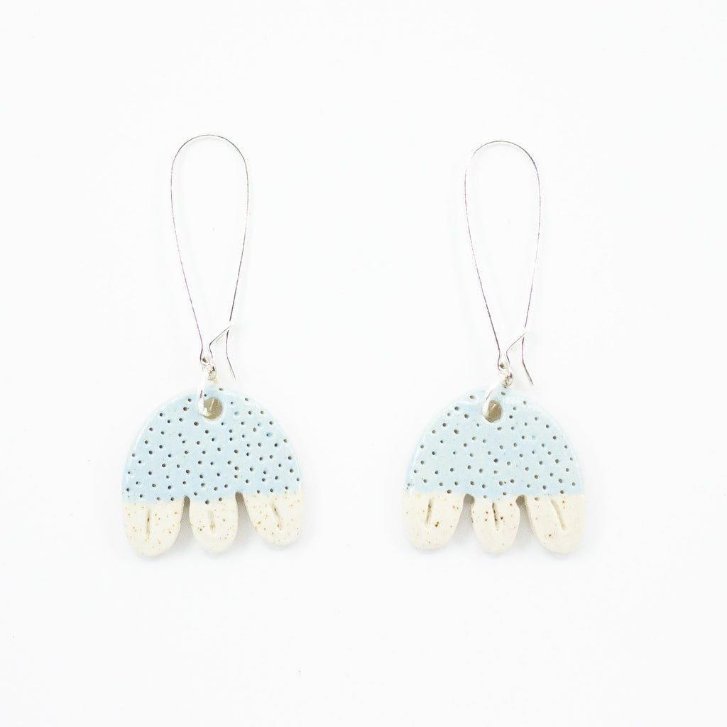 A photo of two ceramic earrings, with sterling silver drop hooks. Ceramic beads are light blue, with polka dot texture, and have 3 natural glazed legs, resembling a jellyfish. 