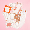 A flat-lay of cute journaling stationery in red, pink and brown tones, featuring designs of notepad pages, a pencil, a flower and a bread slice on a pink background.