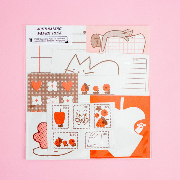 A flat-lay product shot of a 'Journaling Paper Pack' featuring various themed paper sheets with cute illustrations like apples, leaves, and flowers, set against a solid pink background.