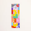 A tall, narrow rectangular bookmark featuring a colourful abstract patchwork design with cartoon-like shapes and blocks in pink, yellow, blue, green, orange, purple, and red, shown against a plain off-white background.