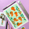 Sheet of illustrated stickers with orange characters on a light green background, surrounded by stationery items on a purple surface.
