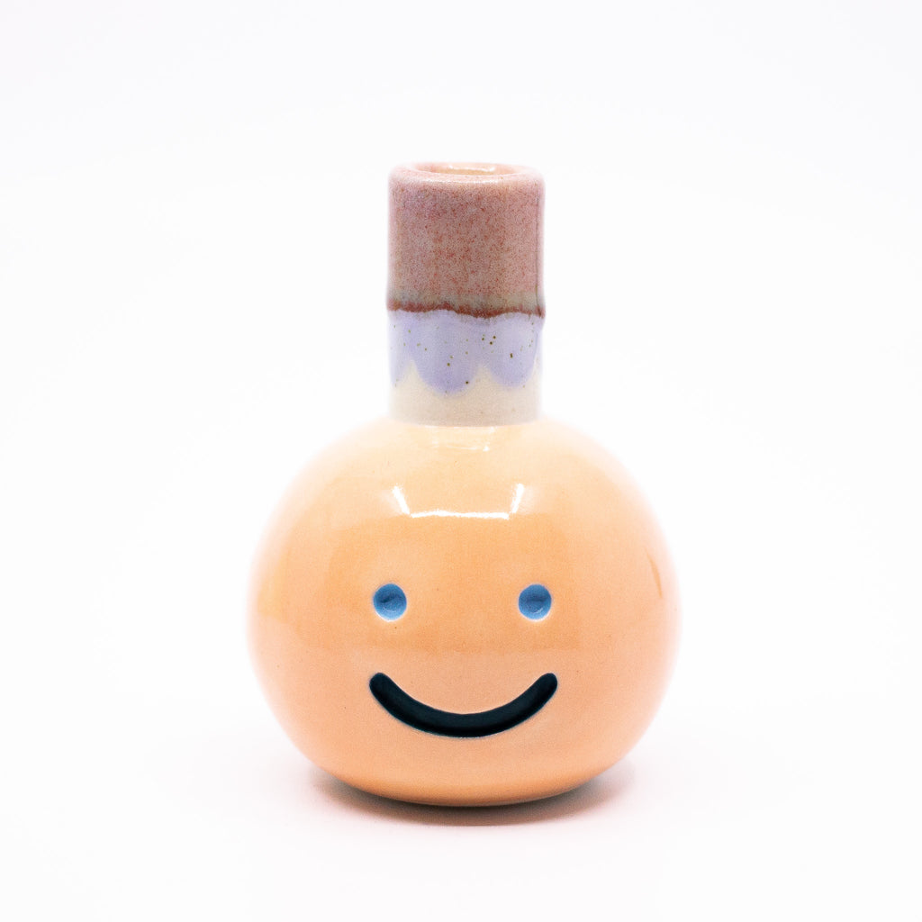 Front view of the Kaori vase. Light orange colour, blue smile, multicoloured spout.
