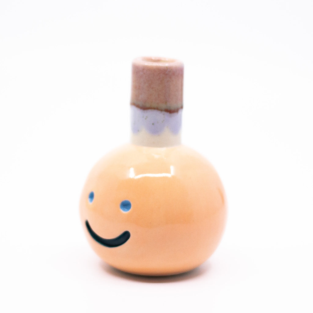 Side view of the Kaori vase. Light orange colour, blue smile, multicoloured spout.
