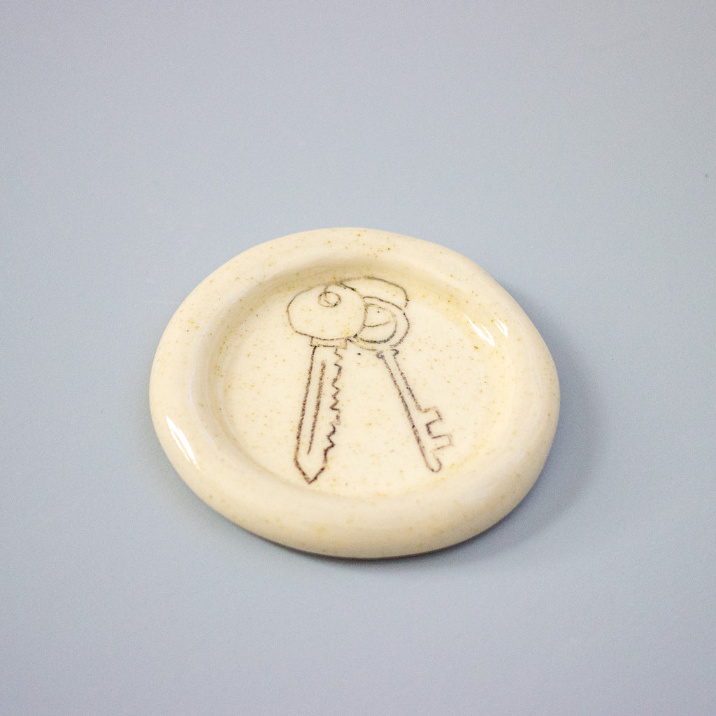 Round ceramic dish with hand drawn keys on a grey background