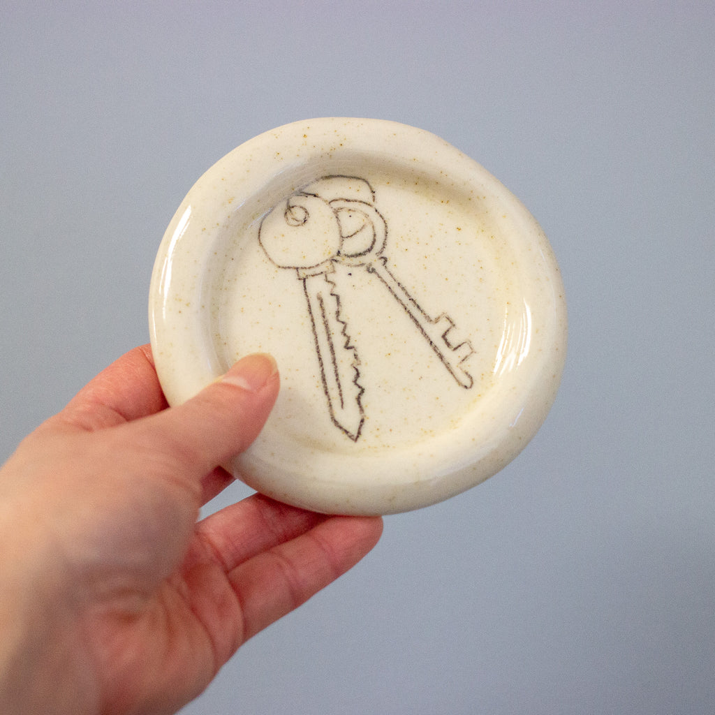 Hand holding a ceramic dish with a key design on a plain background