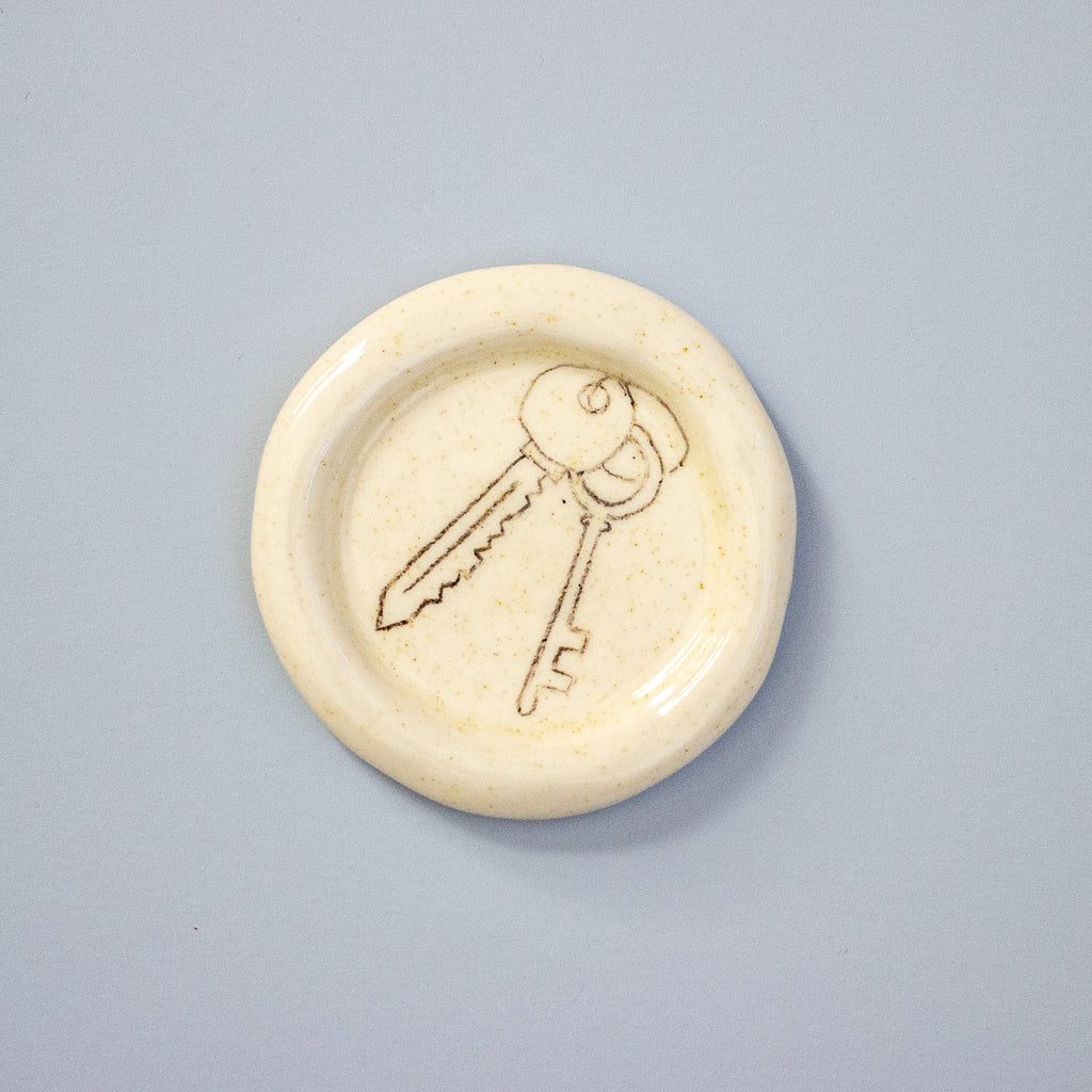 Round ceramic object with a key design on a light grey background