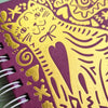 A close-up of a spiral-bound notebook with a textured purple cover decorated with shiny gold foil cat and heart illustrations.