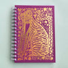 A purple spiral-bound notebook featuring a large gold foil illustration of a cat on the cover, photographed on a light mint green background.