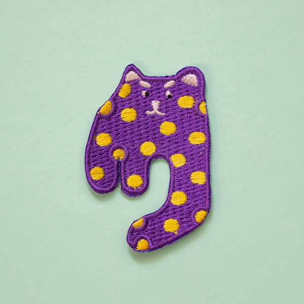 Purple cat-shaped patch with yellow spots on a light green background