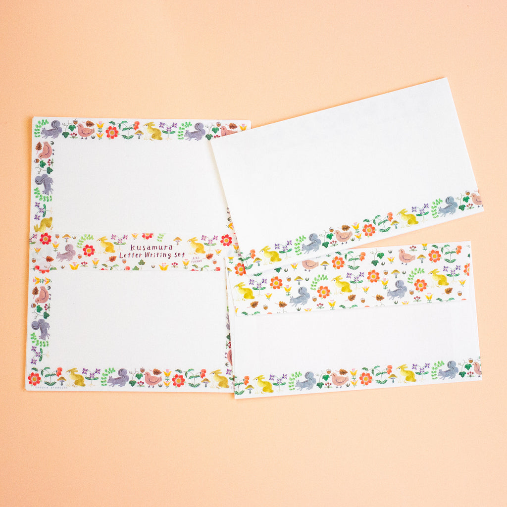 A set of white letter writing paper sheets and envelopes with colourful illustrated borders featuring birds, flowers, and small animals, arranged on a peach background.