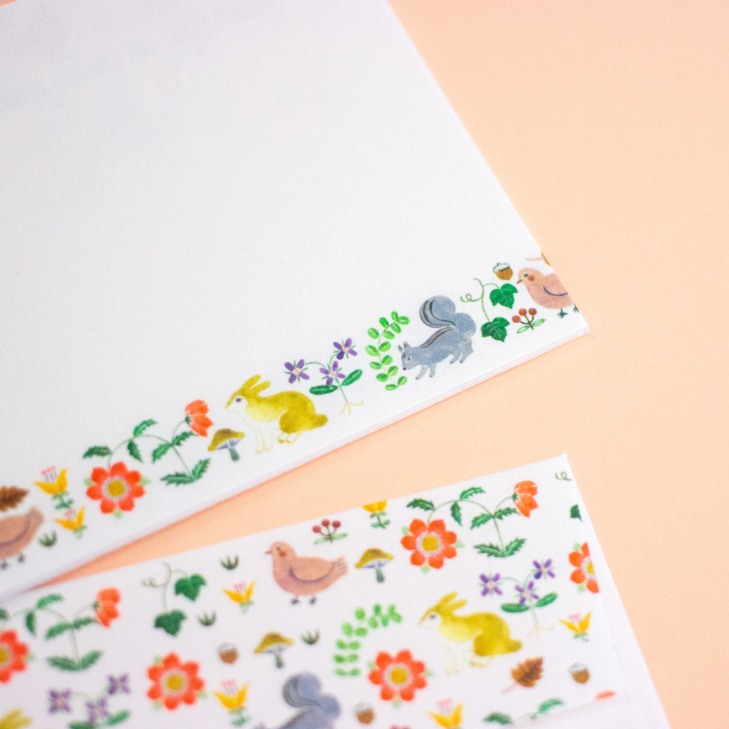 A letterset consisting writing paper sheets and envelopes with colourful illustrated borders featuring birds, and flowers.