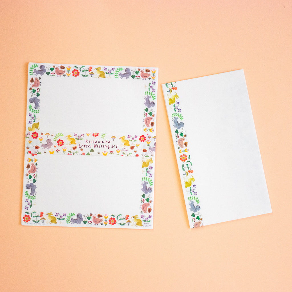 A letterset consisting writing paper sheets and envelopes with colourful illustrated borders featuring birds, flowers, and the text 'kusamura Letter Writing Set' on a peach background.